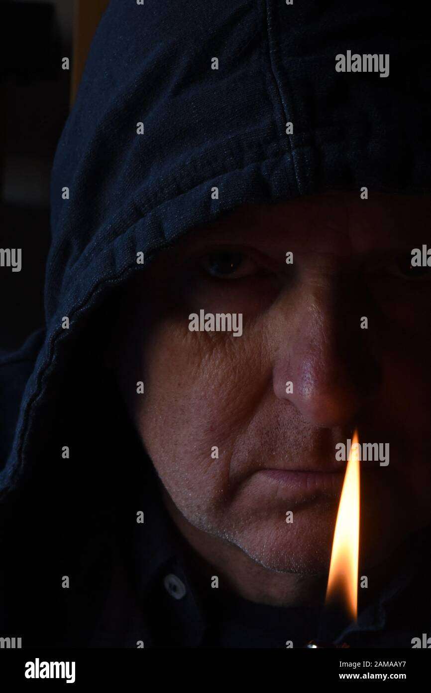 Shadowy close up of older mans face with lighter flame in the foreground Stock Photo