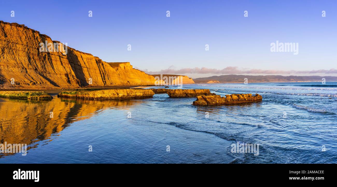 Sunset view of the Pacific Ocean shoreline, with golden colored cliffs reflected on the wet sand, Drakes Beach, Point Reyes National Seashore, Califor Stock Photo