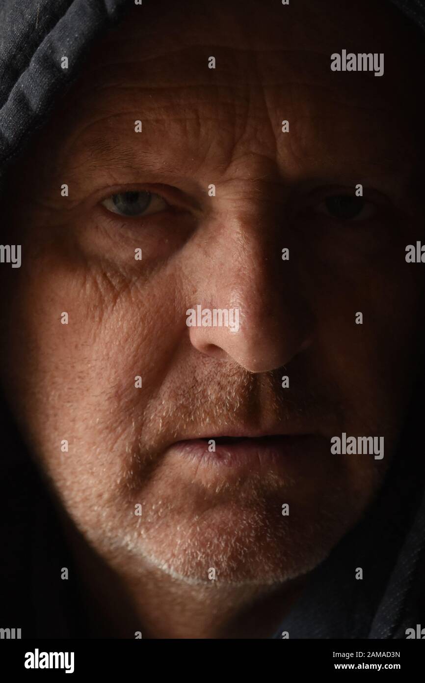 close up of mans face wearing a hoodie., with light from a lighter flame and natural light. Stock Photo