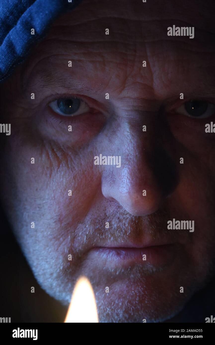 close up of mans face wearing a hoodie., with light from a lighter flame and natural light. Stock Photo
