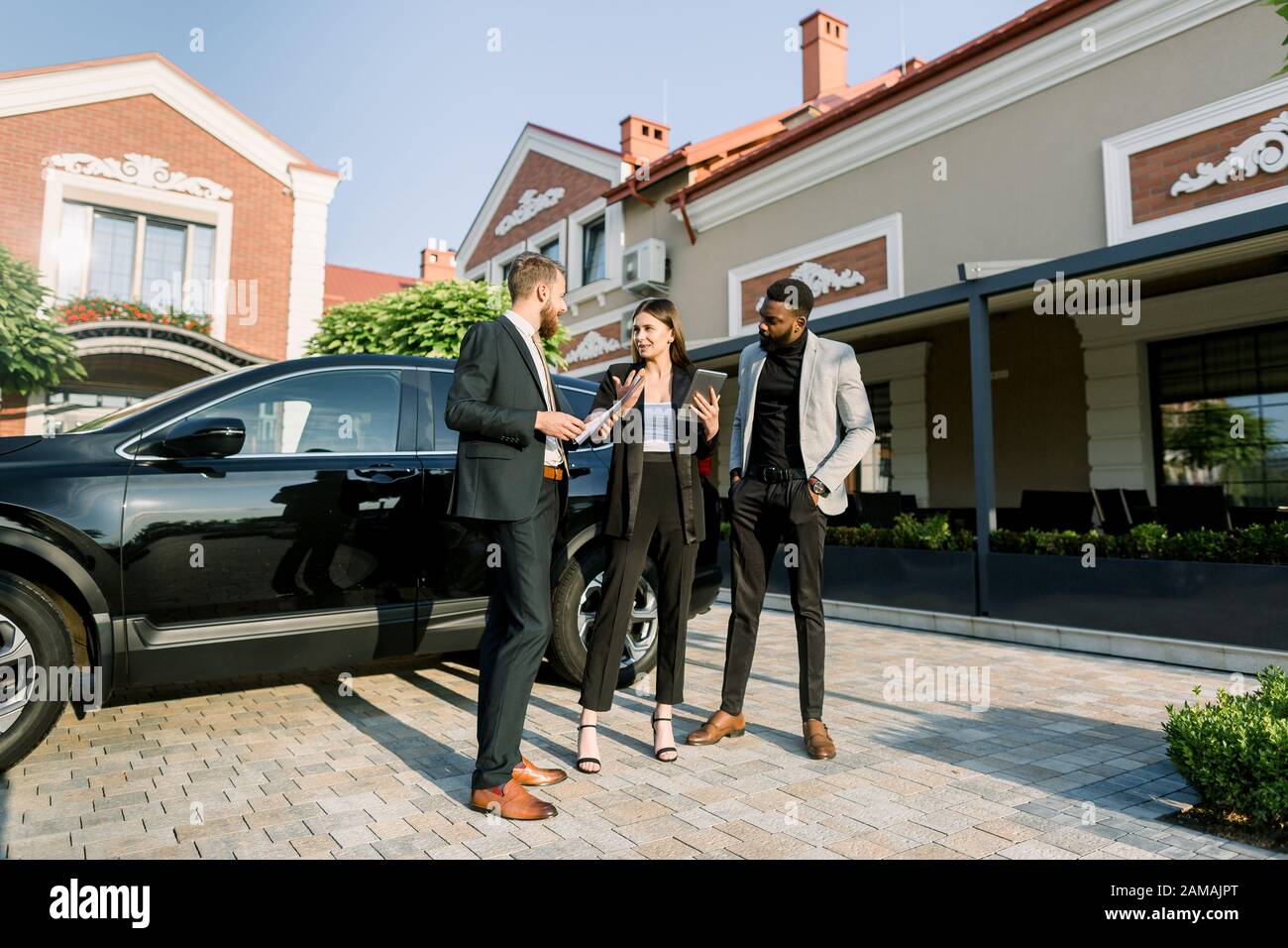 Young Caucasian Man Car Salesman Working With Clients Business Couple African Man And Caucasian Woman In Dealership Outdoors Showing Black New Car Stock Photo Alamy