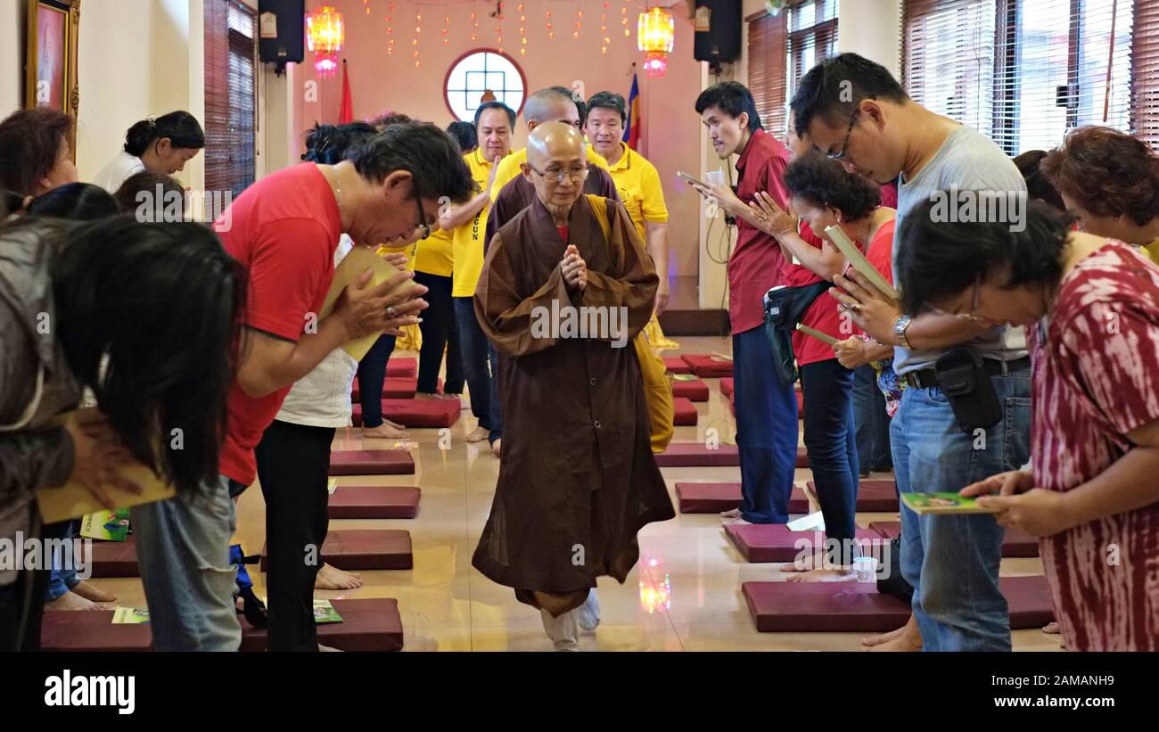 A Buddhist priest walks in a monastery hall while people bowing to him. Stock Photo