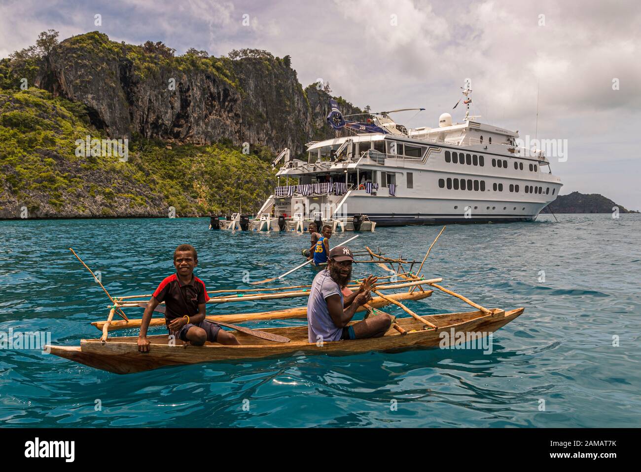 Outrigger Canoe in front of the True North at Panasia Island, Papua New Guinea. Outrigger canoes are not restricted in their maneuverability in the waters above the corals. The True North, on the other hand, must navigate very carefully despite the shallow draft Stock Photo