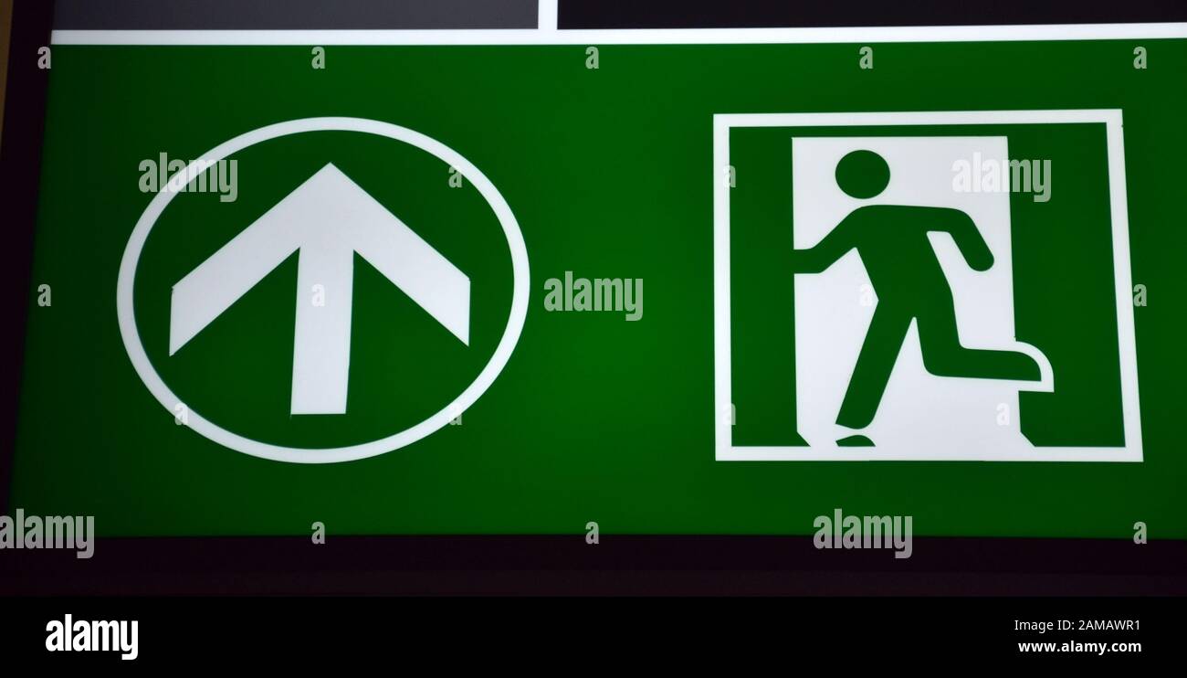 An illuminated green emergency exit sign at an airport shows an image ...