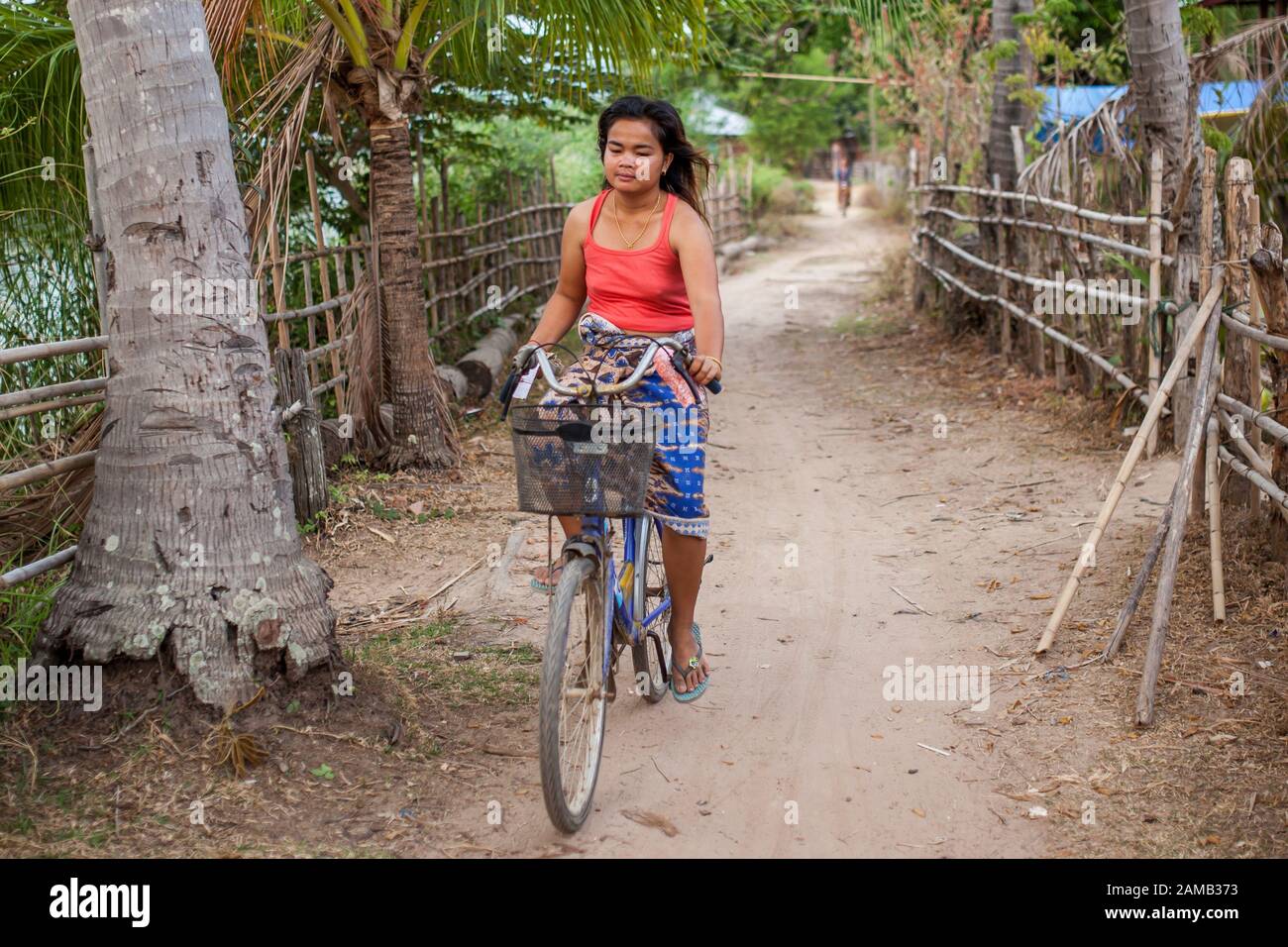 DON DET, LAOS - APRIL 5, 2013: An unidentified girl riding a bicycle through the village of Don Dhet, Laos. Stock Photo
