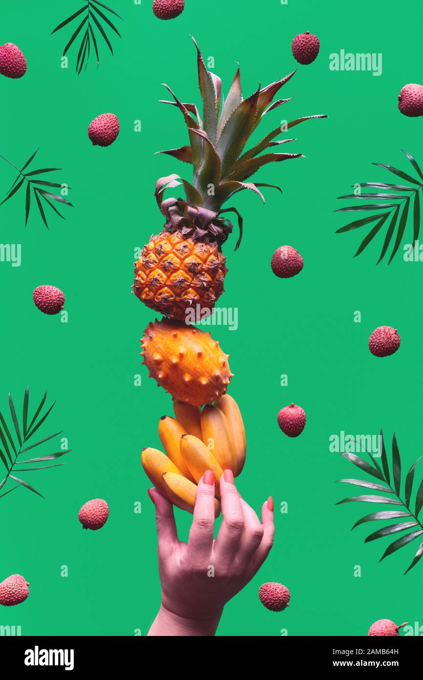 Assortment of tropical fruits, pyramid balancing o human hand on green background. Pineapple, kiwano, kiwi , lichee and banana - tower made of exotic Stock Photo