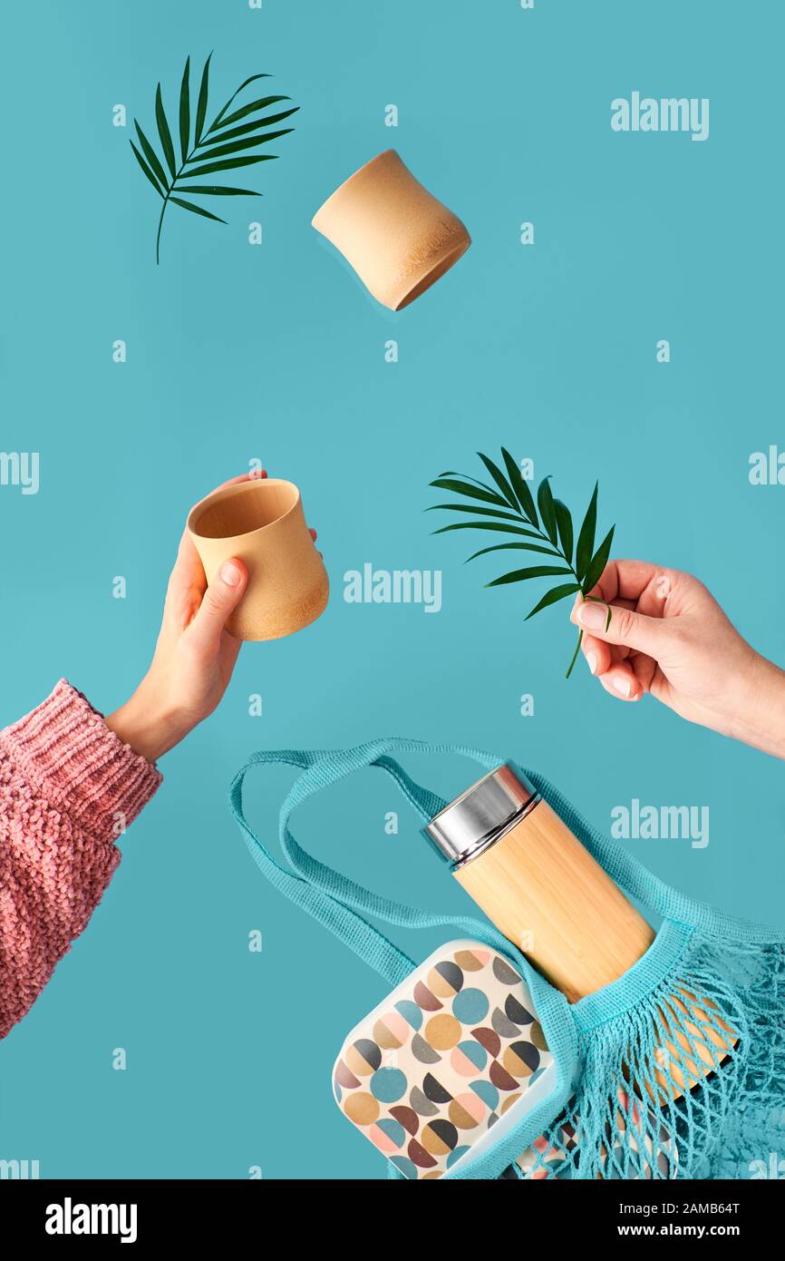 Zero waste tea in in eco friendly insulated bamboo flask. Two hands with cup and palm leaf, net bag with lunch box and tea flask are flying. Zero wast Stock Photo