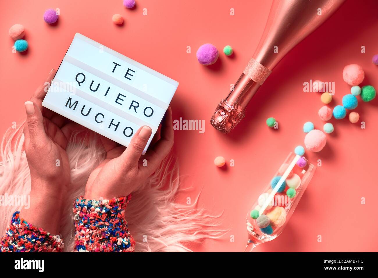 Text 'Te quero mucho' means I love you so much in English. Lightboard with text in Latino female hands, top view on pink background. Bottle of champag Stock Photo