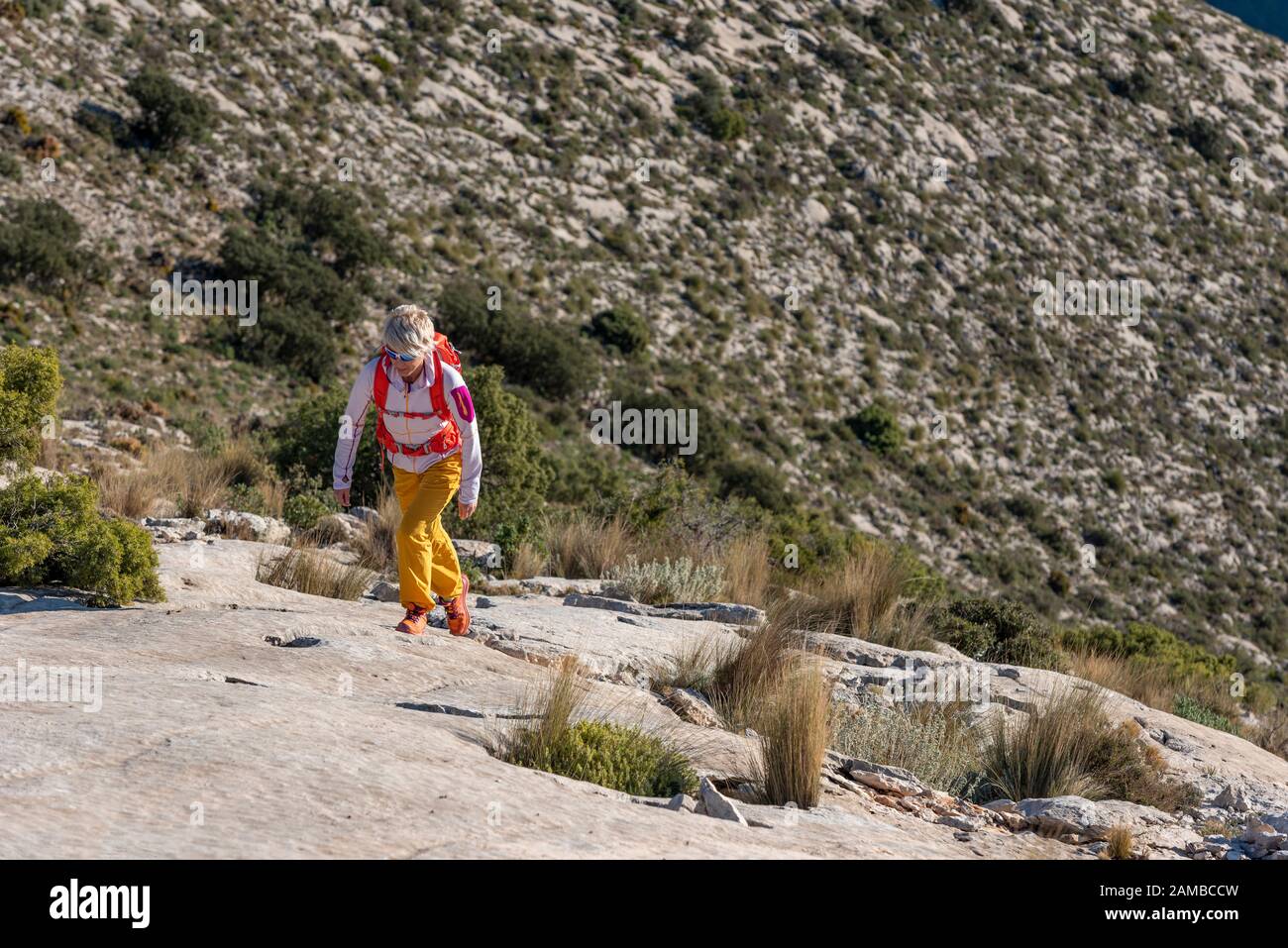 Woman hikes along ridgecrest walks up hill, El Divino mountain, Alicante province, Costa Blanca, Spain Stock Photo