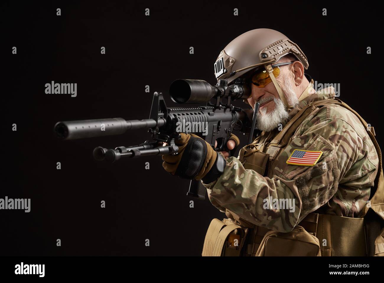 Side view of old military officer holding sniper rifle and aiming. Portrait  of bearded american veteran in uniform and helmet posing with gun on black  studio background. Concept of military Stock Photo -