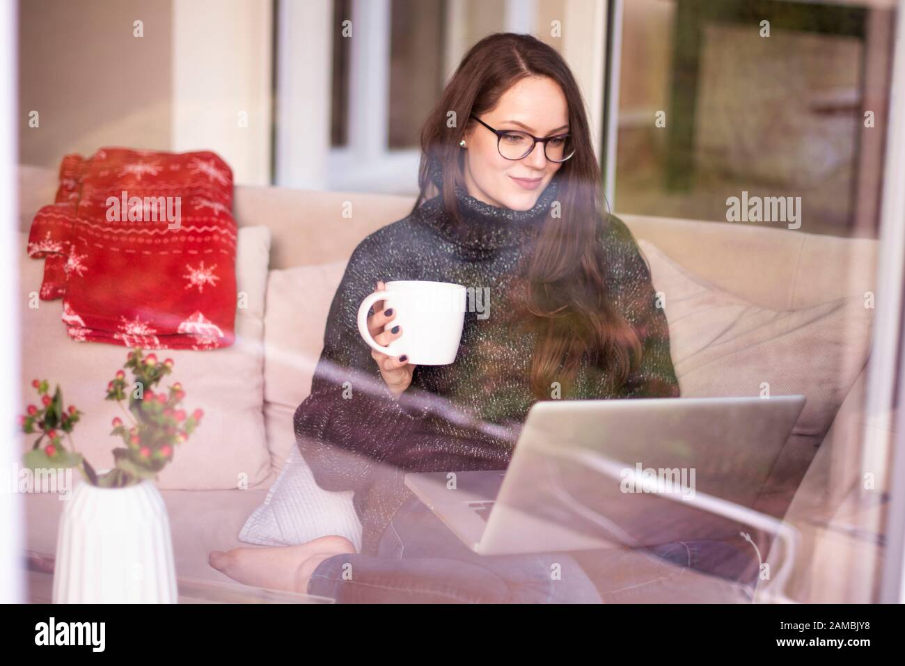 Shot of young woman working on laptop and drinking tea while sitting on ...