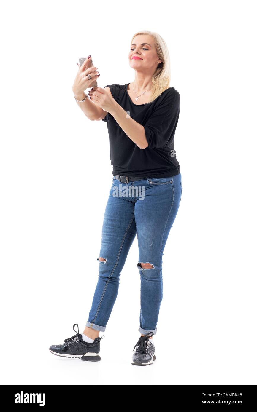 Longsighted middle age casual lady reading cell phone messages holding it at distance. Full body length isolated on white background. Stock Photo