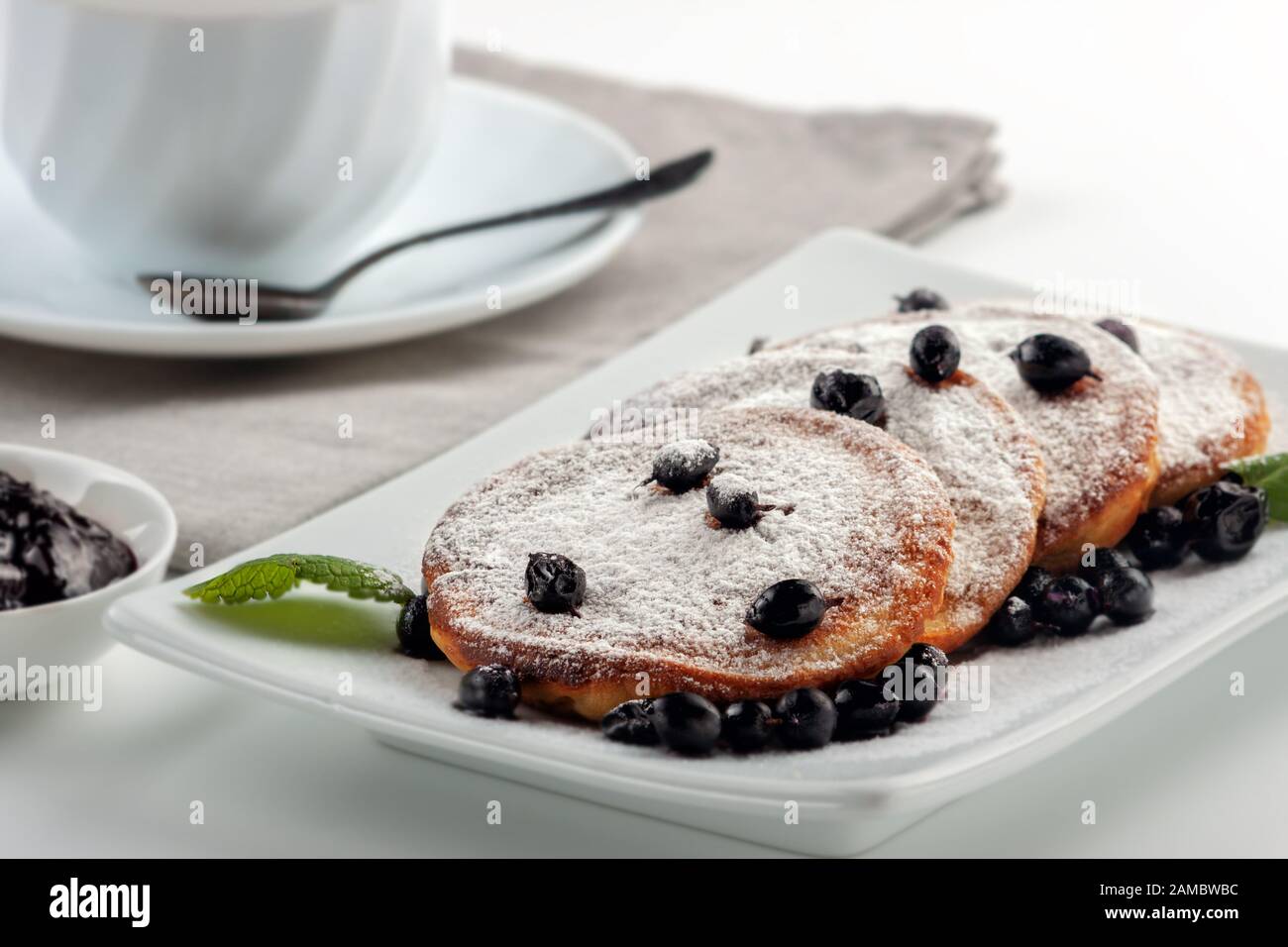 A Cup of coffee with milk and a plate with a pancakes is on the table. Stock Photo