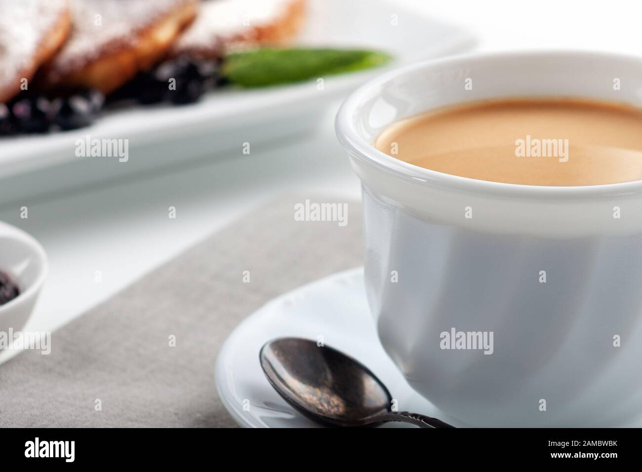 A Cup of coffee with milk and a plate with a pancakes is on the table. Stock Photo