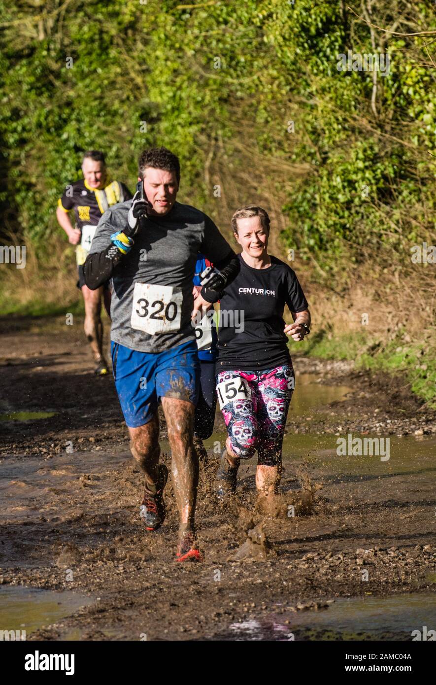 Men and women competition runners running through muddy puddles in a countryside lane on a sunny winter day in January in the UK Stock Photo