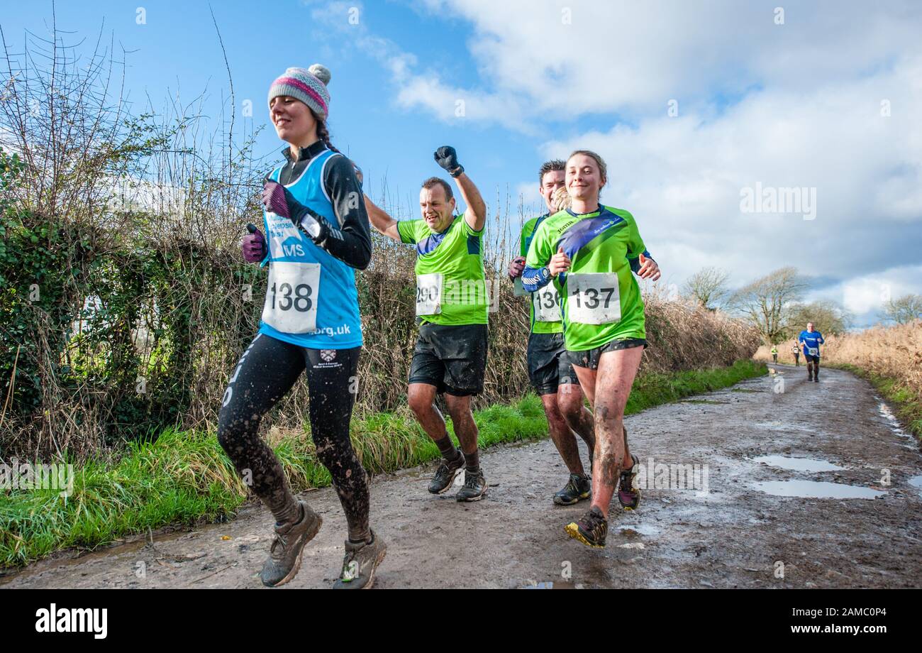 Men and women competition runners running through muddy puddles in a countryside lane on a sunny winter day in January in the UK Stock Photo