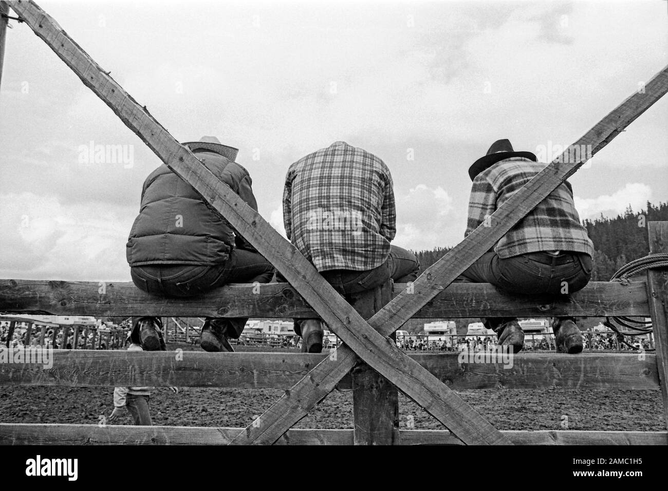 Three rodeo spectators sitting on a wooden fence in rural Canada Monochrome photograph circa 1982. Water Valley Alberta Stock Photo