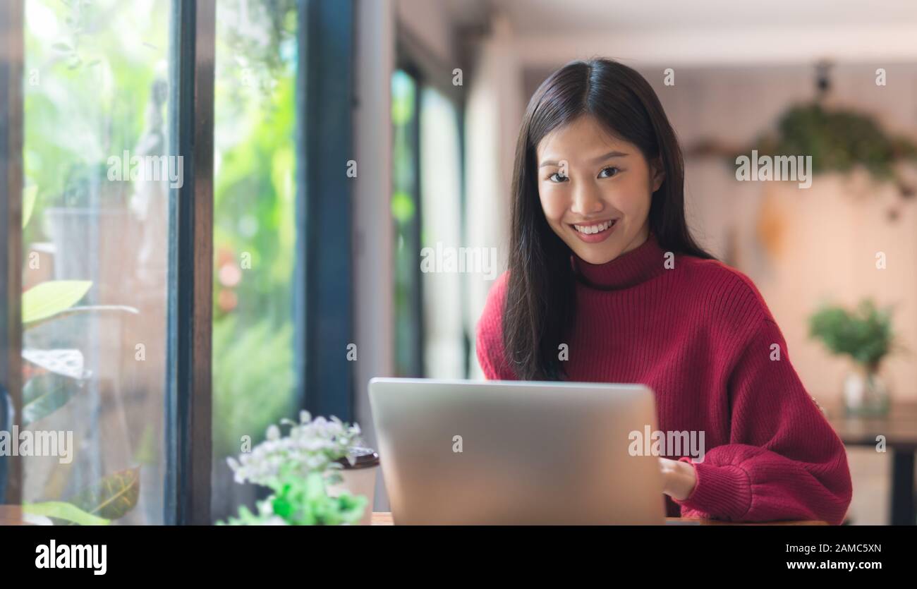 Happy young Asian girl working at a coffee shop with a laptop .Woman happy smiling to camera in cafe day Stock Photo