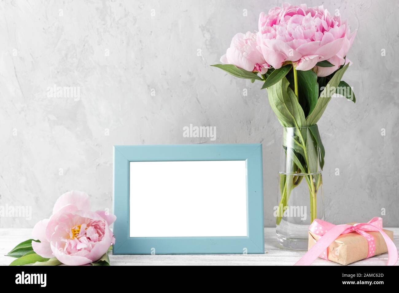 pink pastel peony flowers bouquet with blank photo frame on white table with copy space. mock up. still life. womens day or wedding concept. festive b Stock Photo