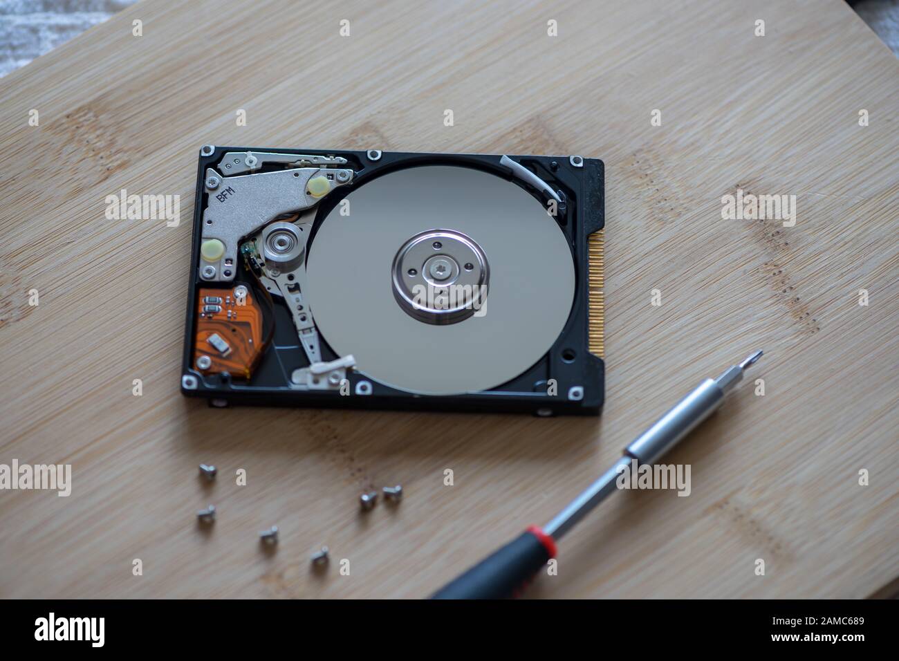 Close-up on a hard notebook disk drive. Opened disk drive with screwdriver on a wooden table. Stock Photo