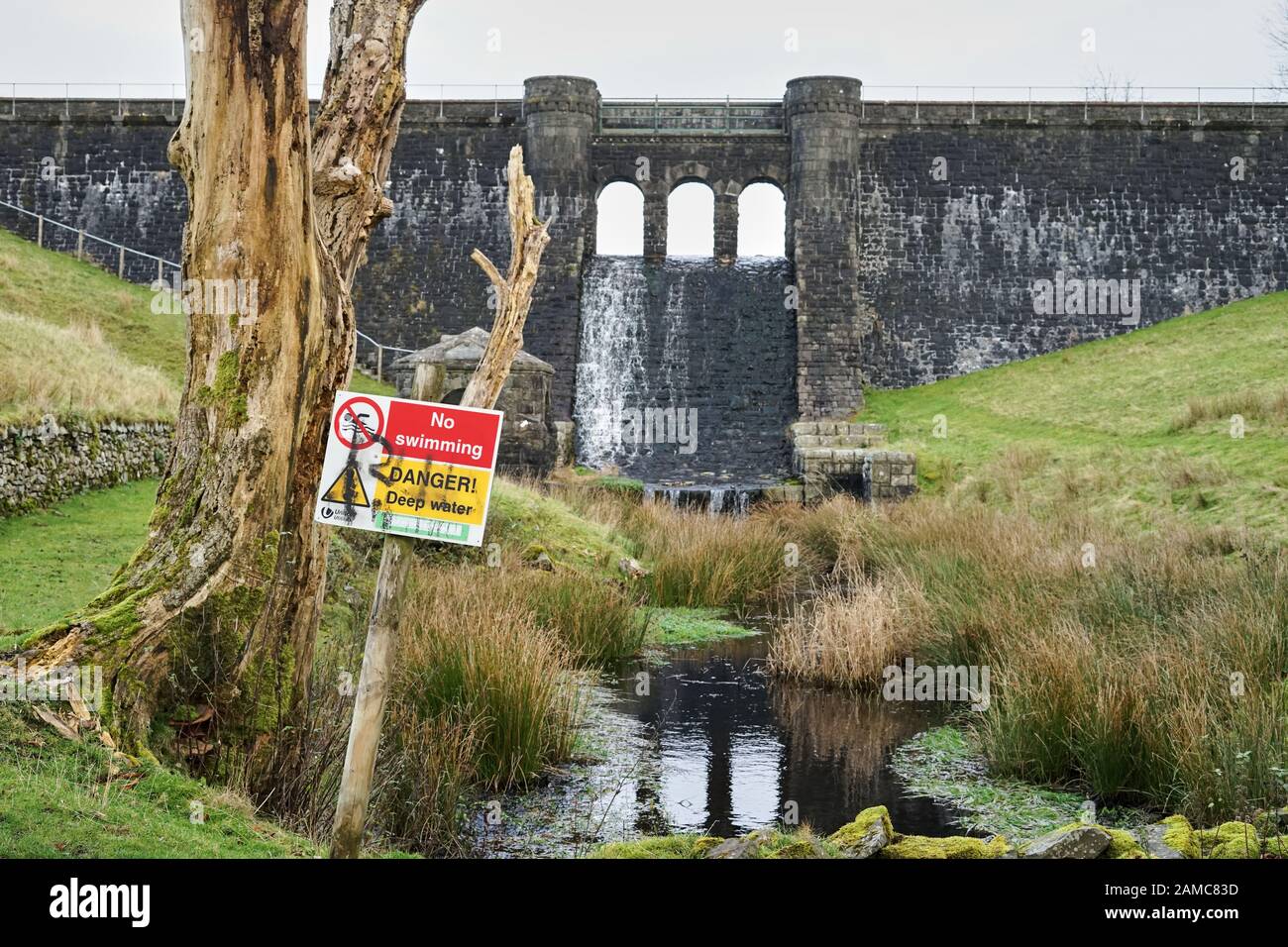 'No swimming' and 'danger deep water' sign in front of a stone dam wall of the Fisher Reservoir, Cumbria, UK Stock Photo