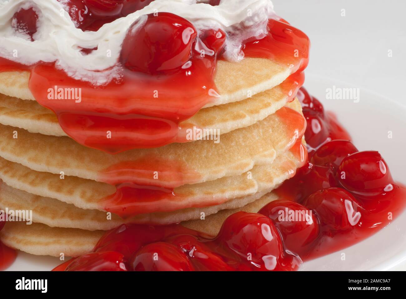 stack of griddle cakes with cherry and whipped cream topping on plate