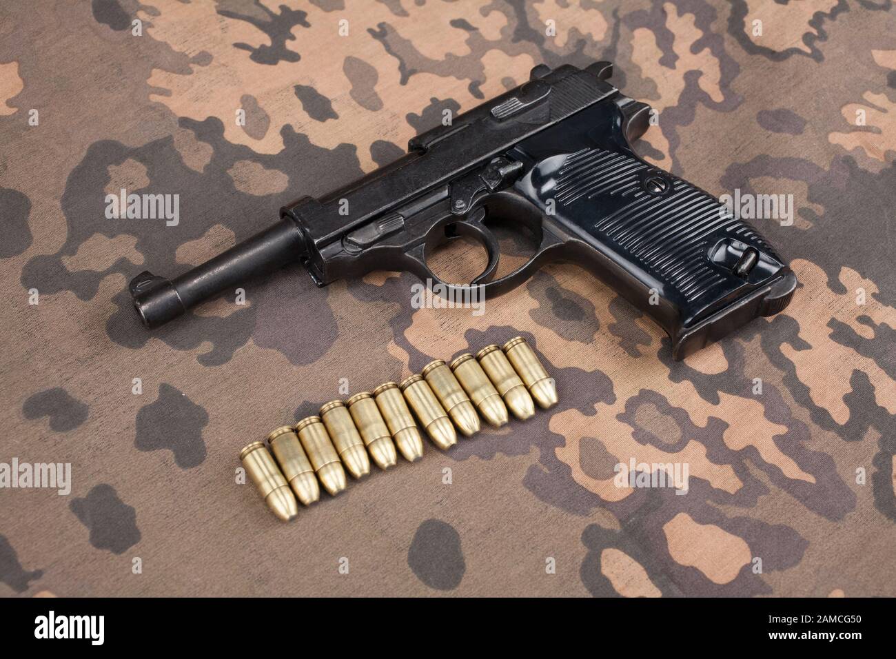 WWII era nazi german army 9 mm semi-automatic pistol with ammunition on camouflaged uniform background Stock Photo