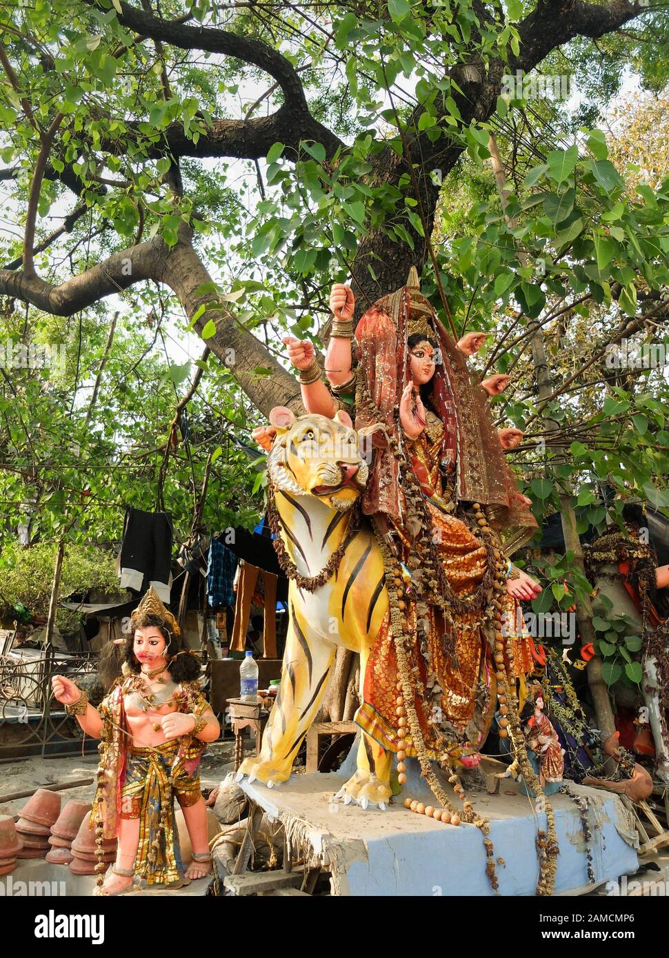 Next to the roadside in the city center,an Indian Godess sits astride a tiger with another female diety sitting below at the foot of the tree,all ador Stock Photo