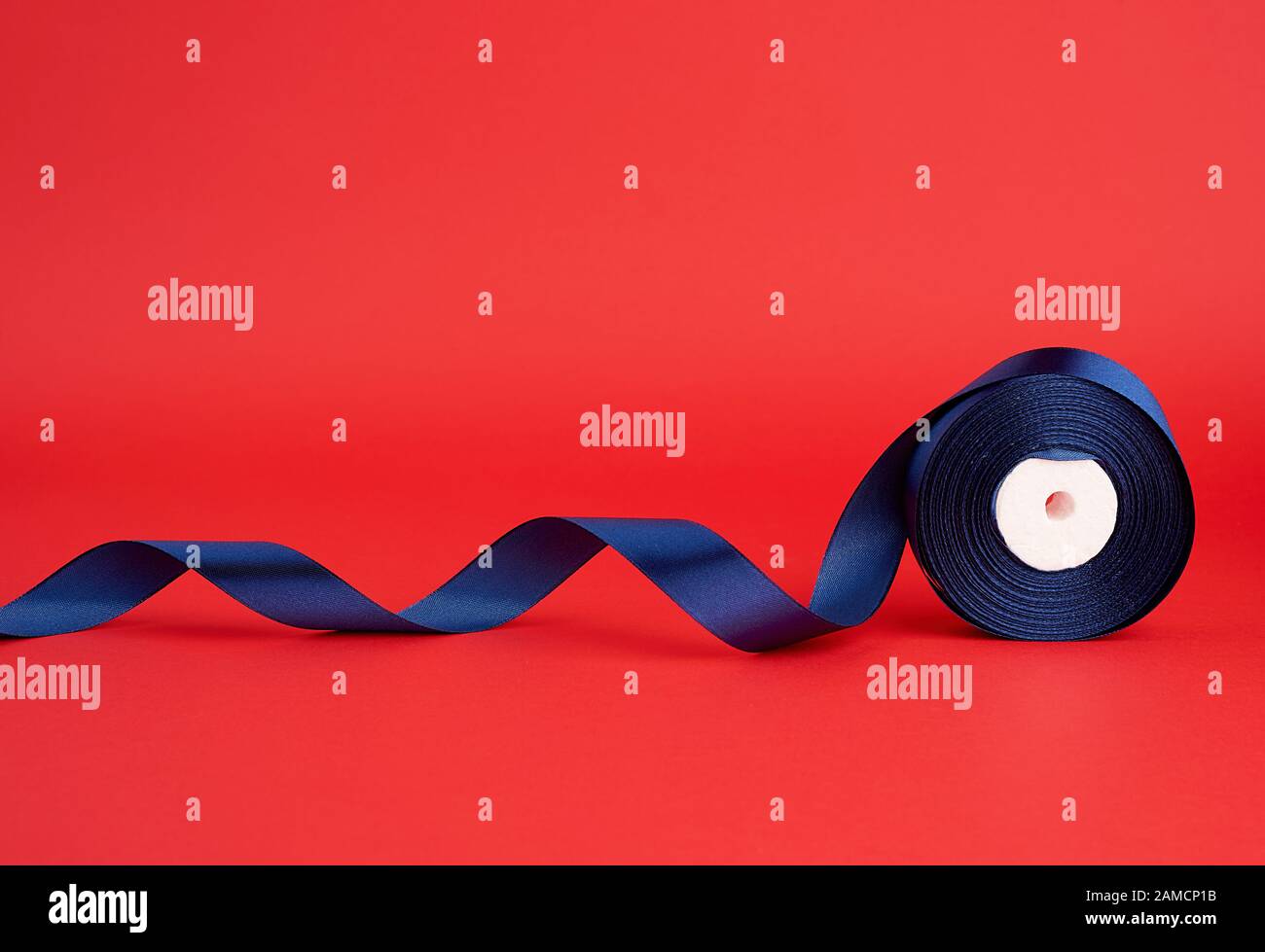spool of twisted dark blue silk shiny ribbon on a red background ...