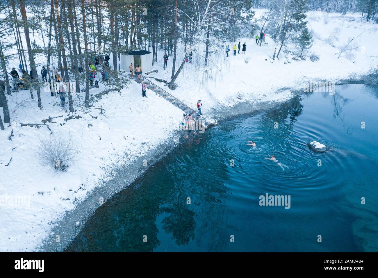 Altai, Russia - 03.01.2020: Aerial view of people bathing in an icy and cold blue lake with snow in the winter in the mountains during wellness and ba Stock Photo