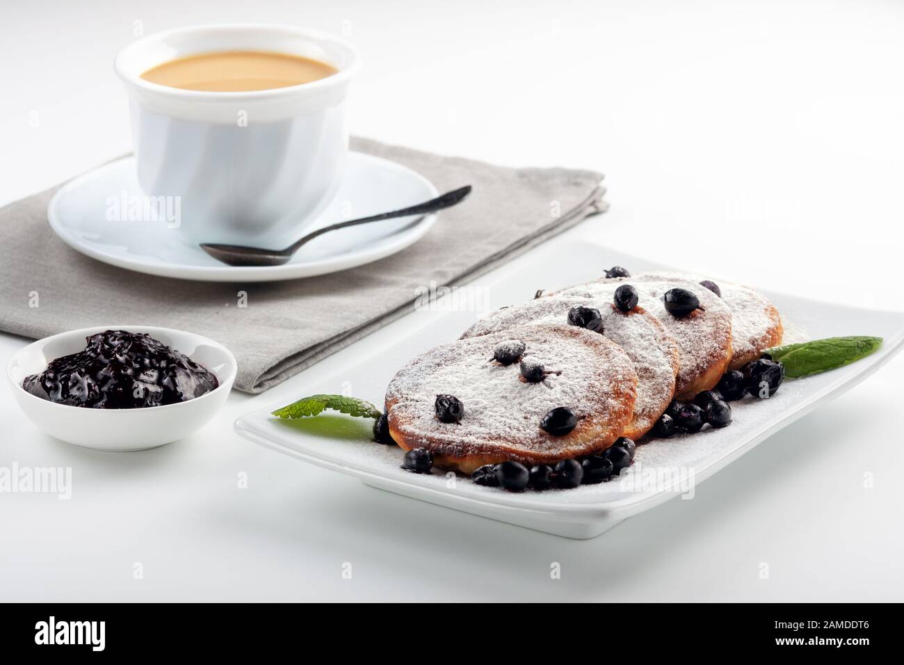 A Cup of coffee with milk and a plate with a pancakes is on the table. Stock Photo