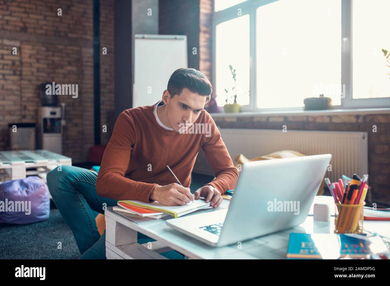 Dark-haired student making notes while watching educational video Stock Photo