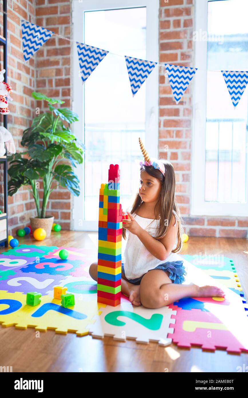 Adorable toddler playing with building blocks toy around lots of toys