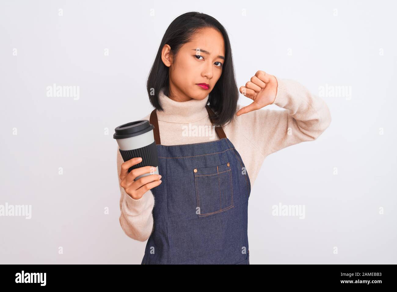 Beautiful barista chinese woman wearing apron holding coffee over isolated white background with angry face, negative sign showing dislike with thumbs Stock Photo
