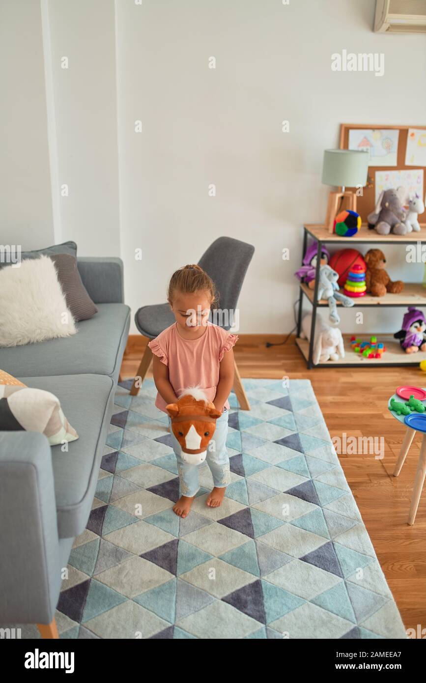 Beautiful blond toddler girl ridding horse with stick toy at kindergarten Stock Photo