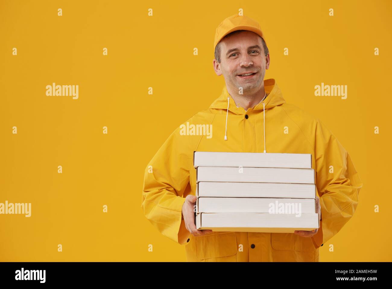 Waist up portrait of adult delivery man holding pizza boxes and smiling at camera standing against pop yellow background, copy space Stock Photo