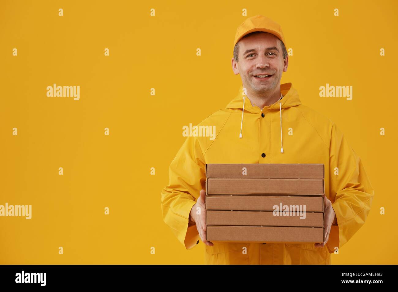 Waist up portrait of adult delivery man holding pizza boxes and smiling at camera while standing against pop yellow background, copy space Stock Photo