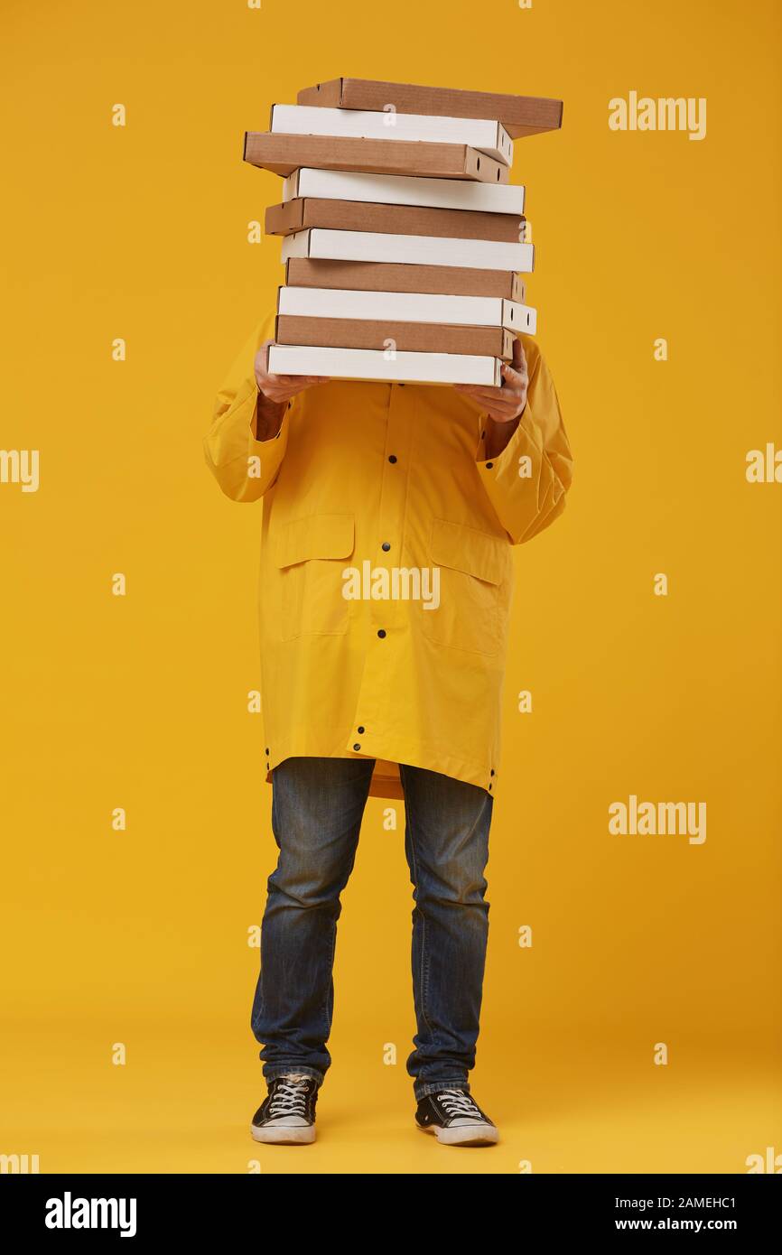 Full length portrait of unrecognizable delivery man hiding behind pizza boxes while standing against pop yellow background in studio Stock Photo