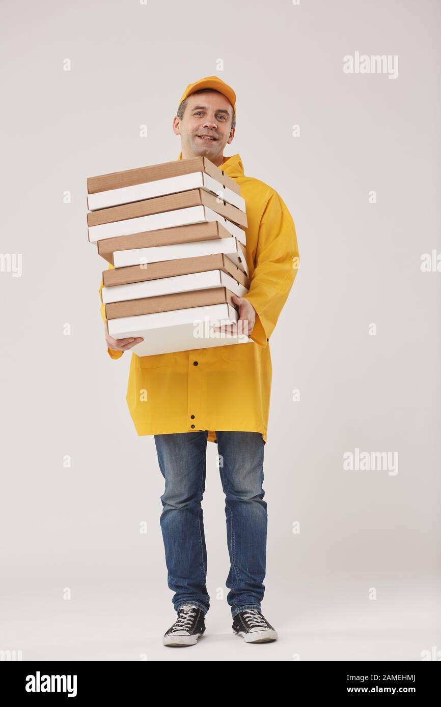 Full length portrait of adult delivery man holding pizza boxes and smiling cheerfully at camera while standing against white background Stock Photo