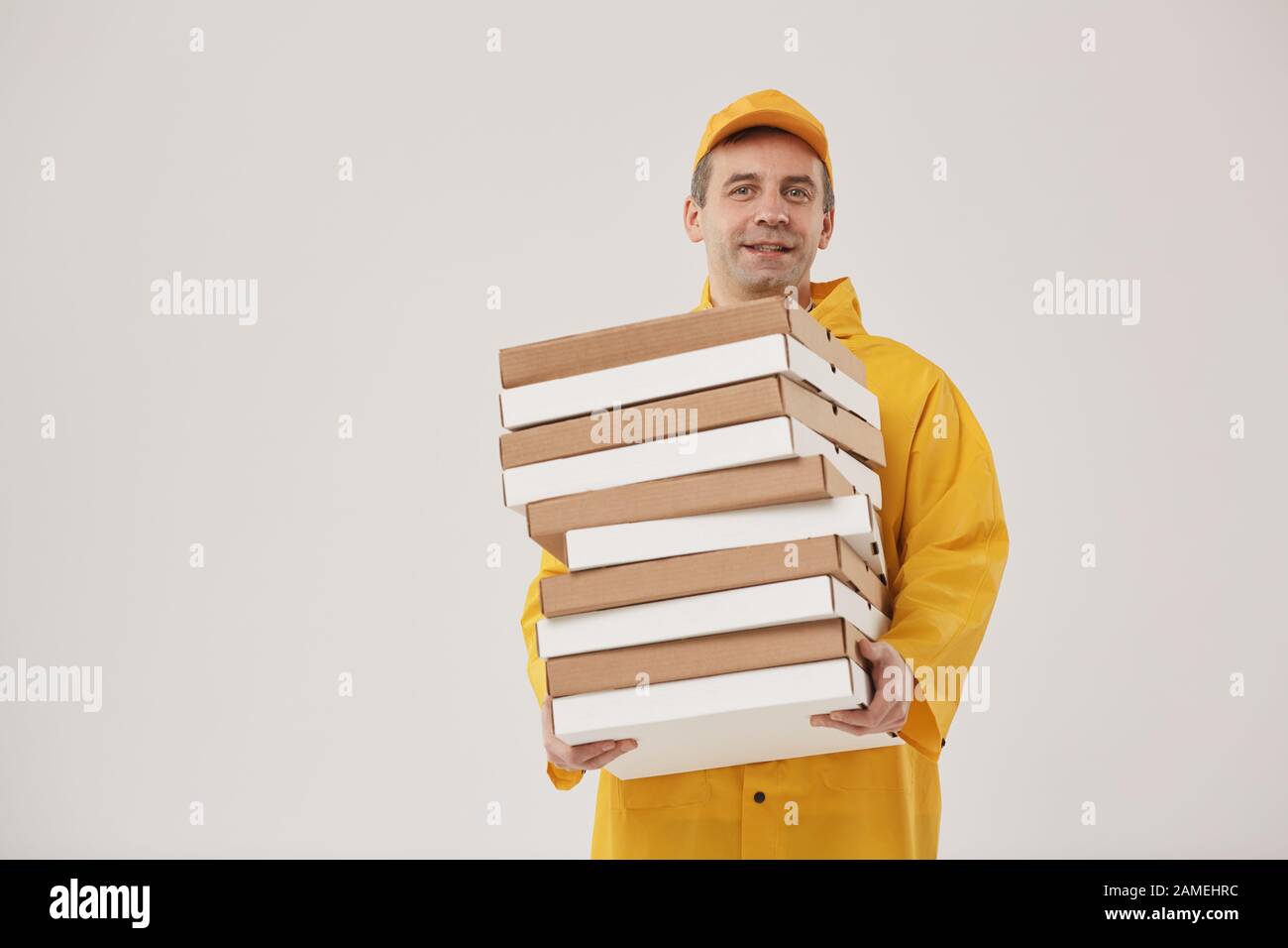 Waist up portrait of adult delivery man holding pizza boxes and smiling cheerfully at camera while standing against white background, copy space Stock Photo