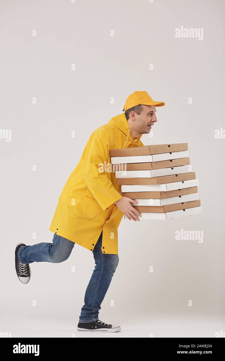 Side view full length portrait of adult delivery man holding stack of pizza boxes while running against white background, fast food service Stock Photo