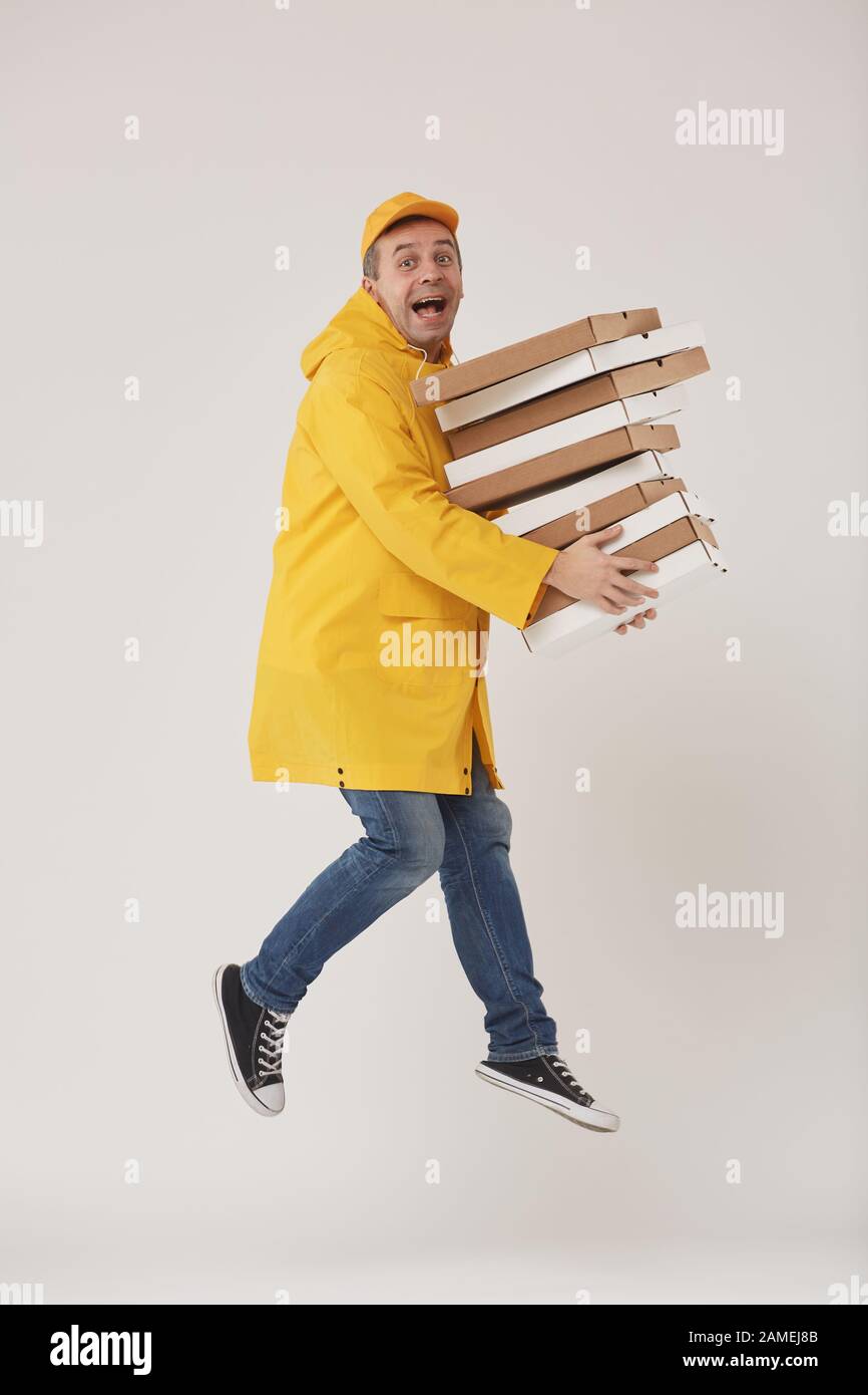 Full length portrait of animated delivery guy jumping high holding pizza boxes against white background, super fast food service Stock Photo