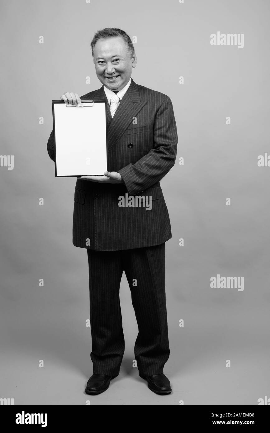 Studio shot of mature Asian businessman holding clipboard against gray ...