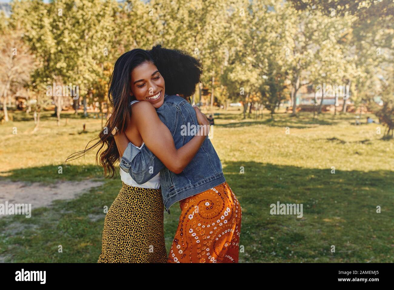 Close-up of two multiethnic happy pretty woman friends hugging each other in the park Stock Photo