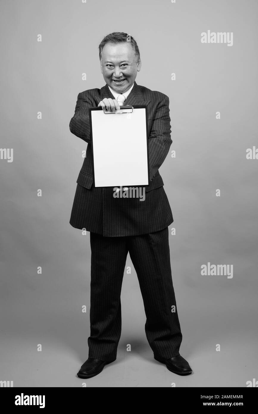 Studio shot of mature Asian businessman holding clipboard against gray ...