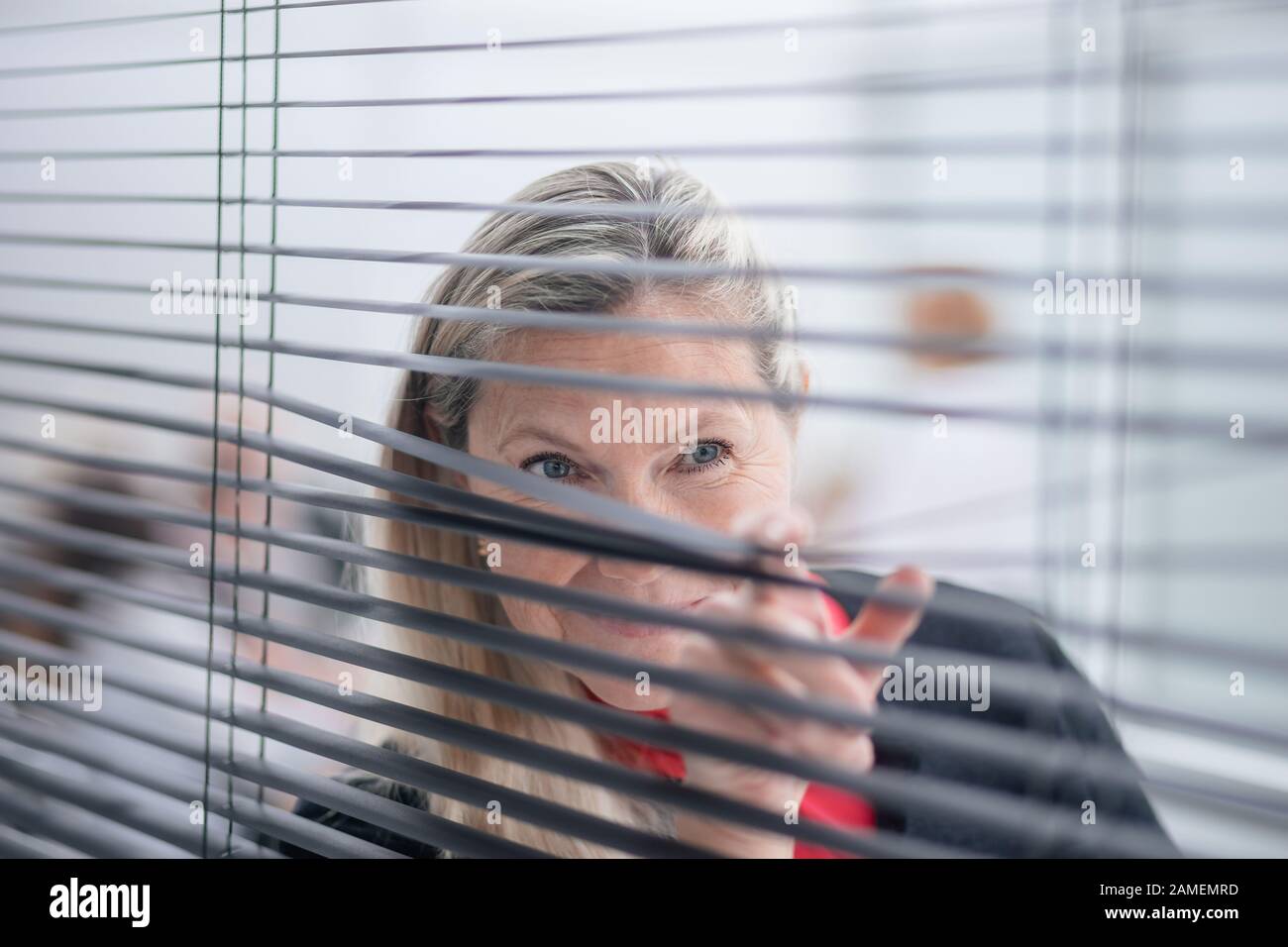 smiling-businesswoman-looking-through-office-window-blinds-stock-photo