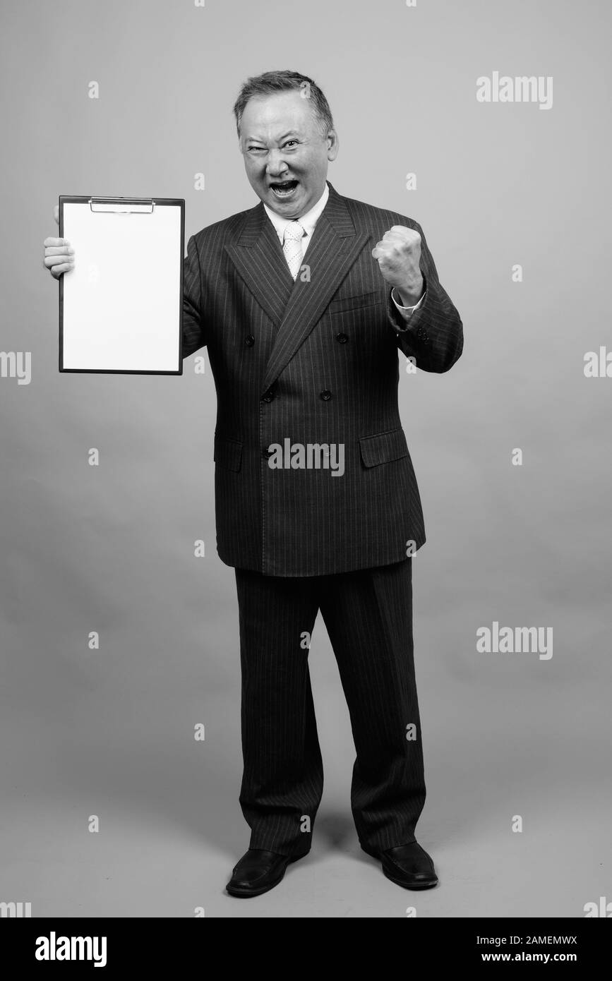 Studio shot of mature Asian businessman holding clipboard against gray ...