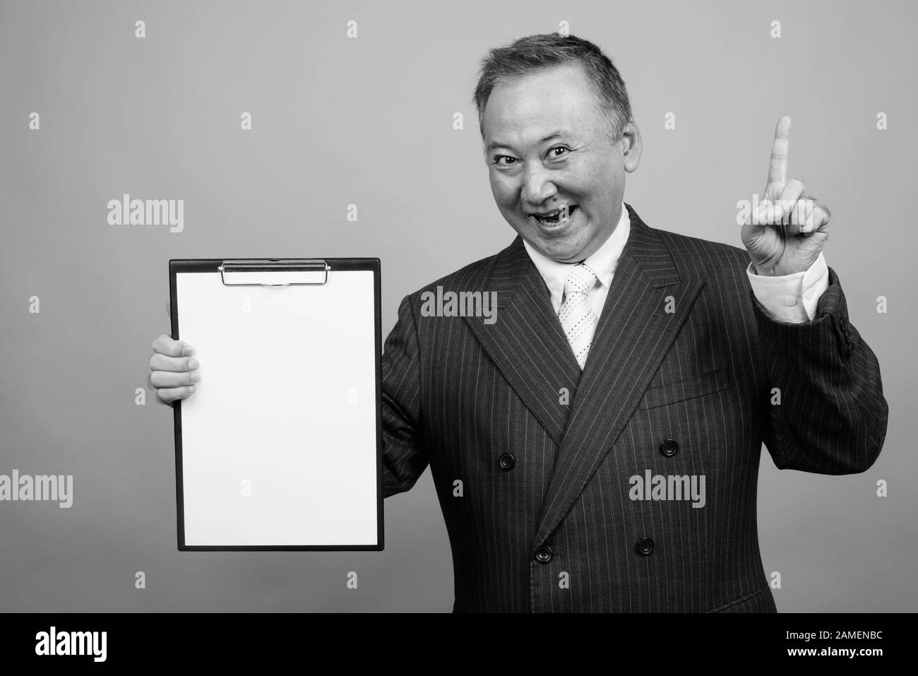 Studio shot of mature Asian businessman holding clipboard against gray ...