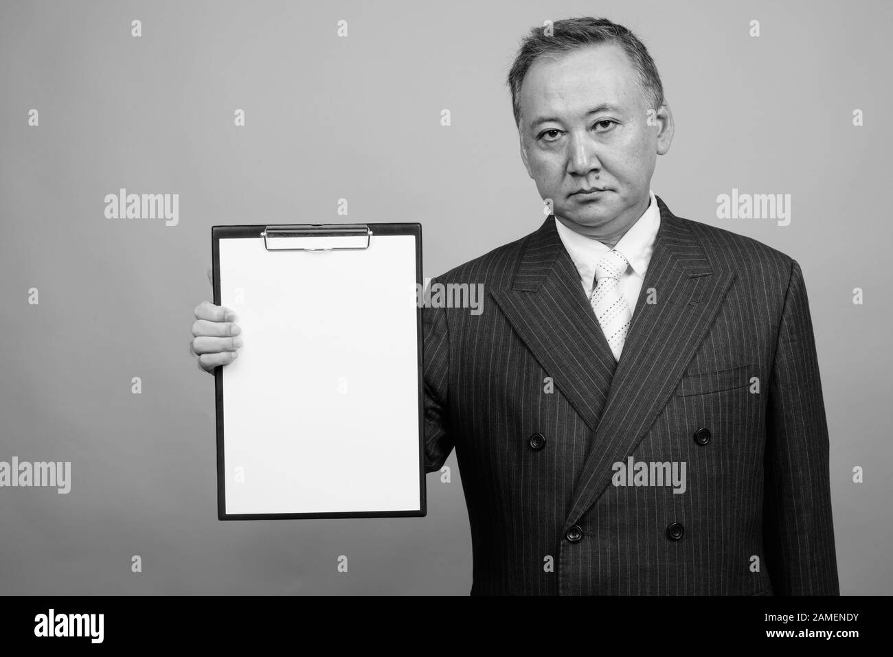 Studio shot of mature Asian businessman holding clipboard against gray ...