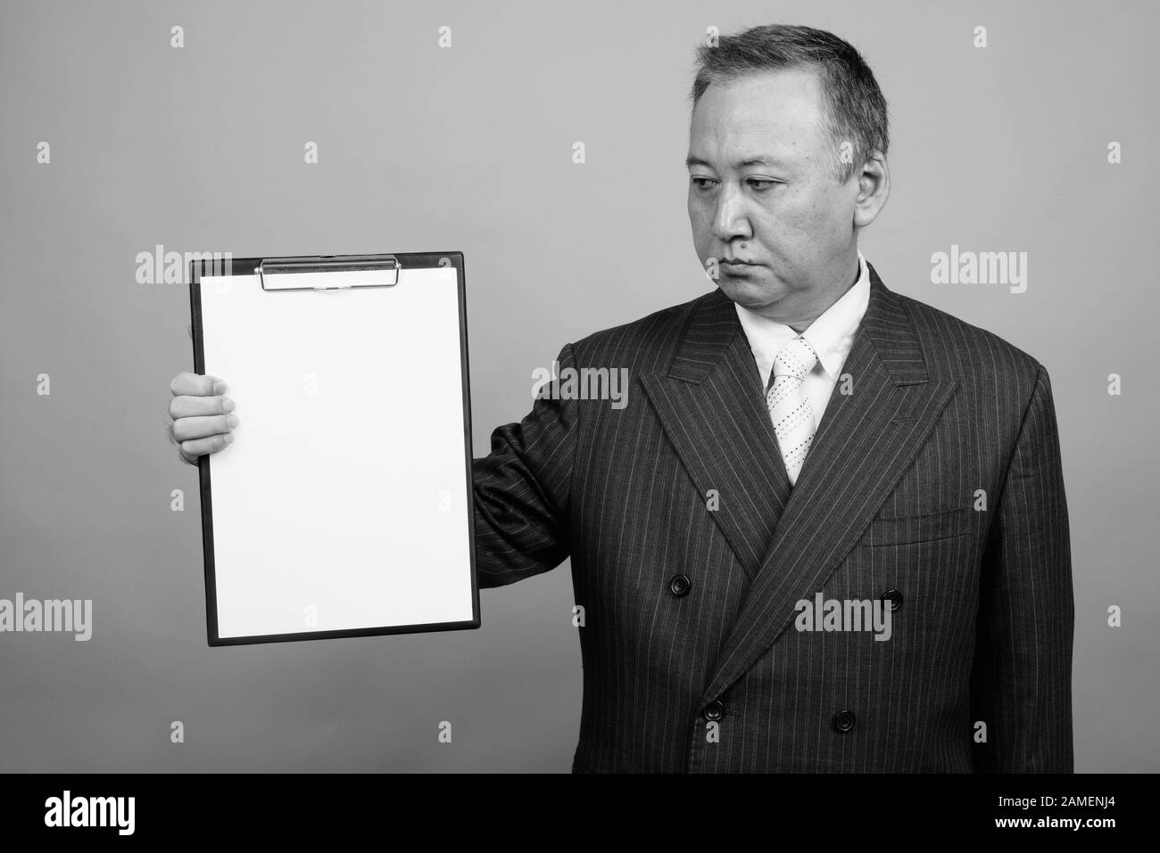 Studio shot of mature Asian businessman holding clipboard against gray ...